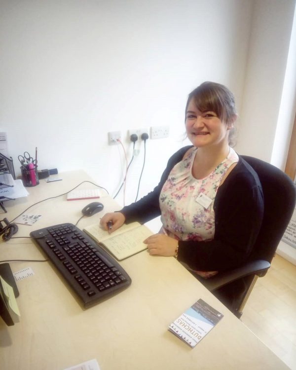 Picture: Shona MacMillan sitting at a desk, smiling at the camera with a notebook and keyboard in front of her