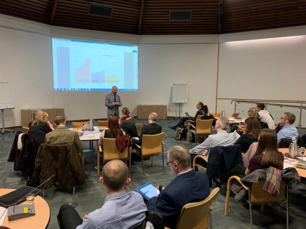 Picture: Jim Whannel, Director of Education, standing in front of a room full of seated teachers at round tables, with a large whiteboard projected behind him, showing some graphs