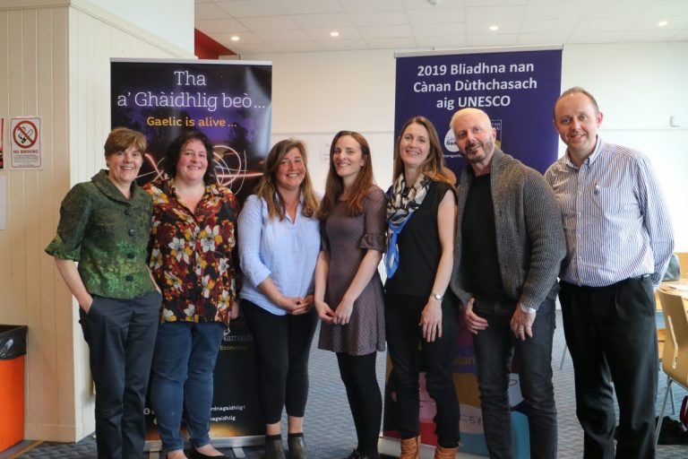 Picture: Seven people, including members of the Bòrd na Gàidhlig Leadership Team and Board, standing in front of a banner reading "Tha Gàidhlig beò/Gaelic is alive..." and another banner reading "2019 Bliadhna nan Cànan Dùthchasach aig Unesco/2019 Unesco Years of Minority Languages"