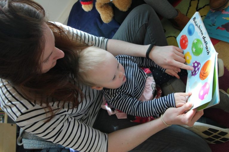 Picture: A mother sitting on the floor with a baby in her lap, reading a book together 