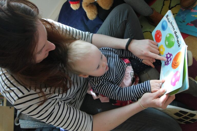 Picture: A mother sitting on the floor with a baby in her lap, reading a book together 