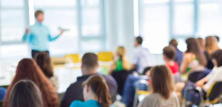 Picture: A blurred image of a person addressing standing in front of a room of people