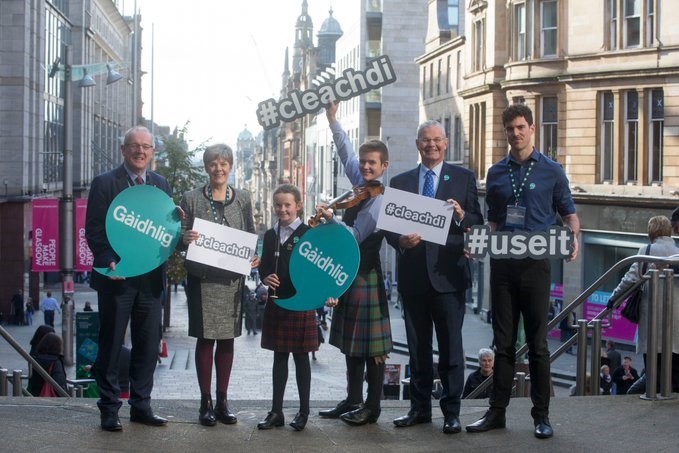 Picture: Six people standing at the steps of the Royal Concert Hall in Glasgow, holding props that read "Gàidhlig", "#cleachdi", "#useit"