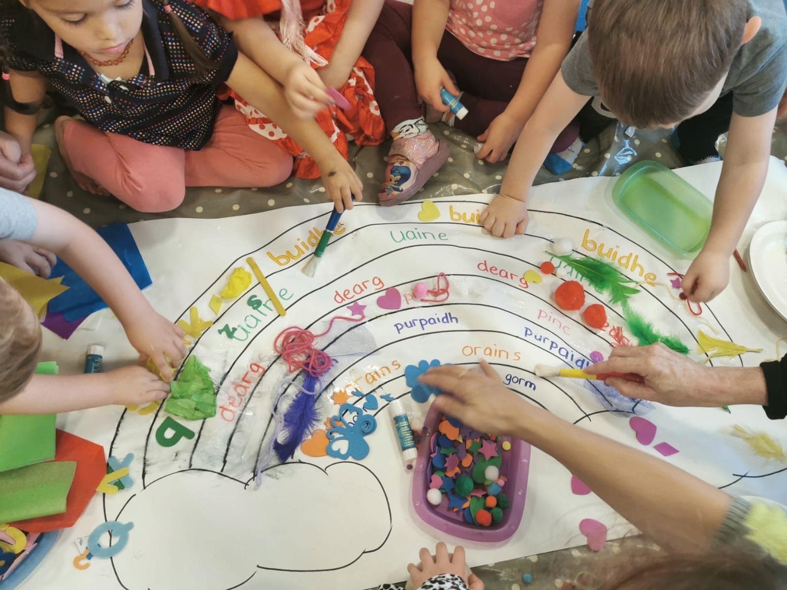 Picture: Children around a large piece of paper doing an activity on the colours of the rainbow in Gaelic, sticking different things on to match each colour.