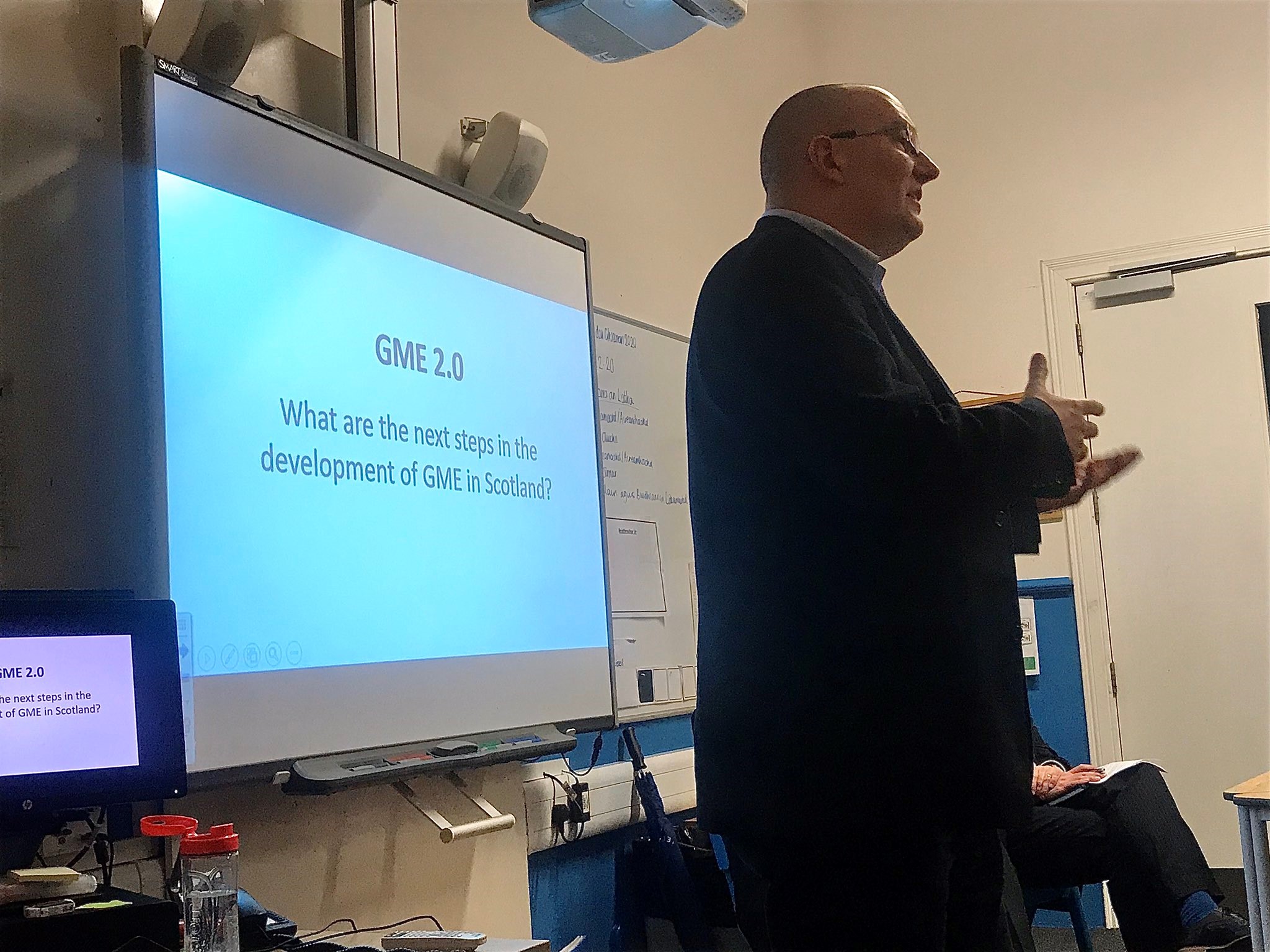 Picture: Man with glasses standing in front of smartboard with "GME 2.0 What are the next steps in the development of GME in Scotland?"