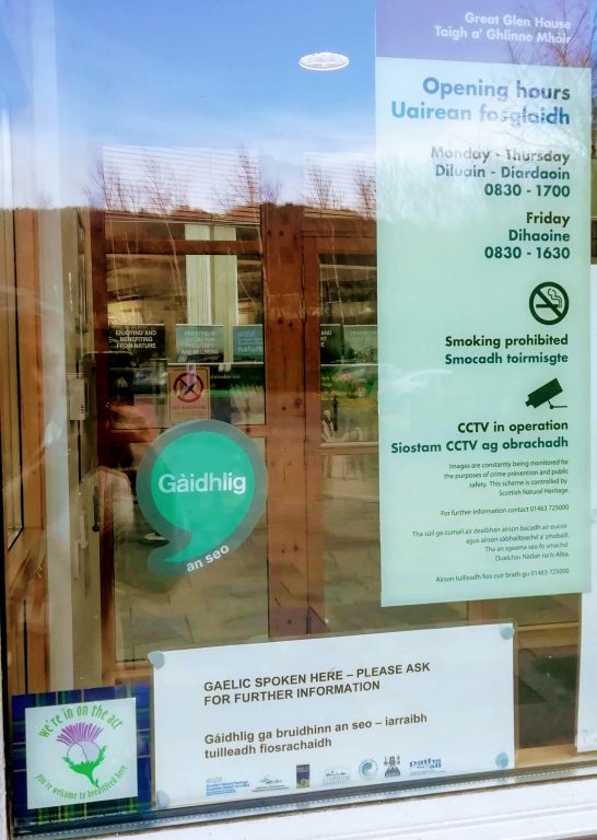 Picture: A window with a cleachdi sticker in it, a notice that Gaelic is spoken here and opening hours