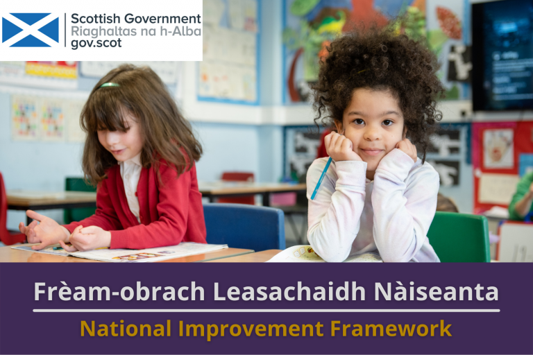 Picture: Two primary school pupils sitting at their desk in a classroom. Text reads 'National Improvement Framework'.