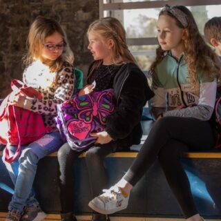 Picture: Three young girls sitting on the edge of the stage in Sabhal Mòr Ostaig's Talla Mhòr (Big Hall)